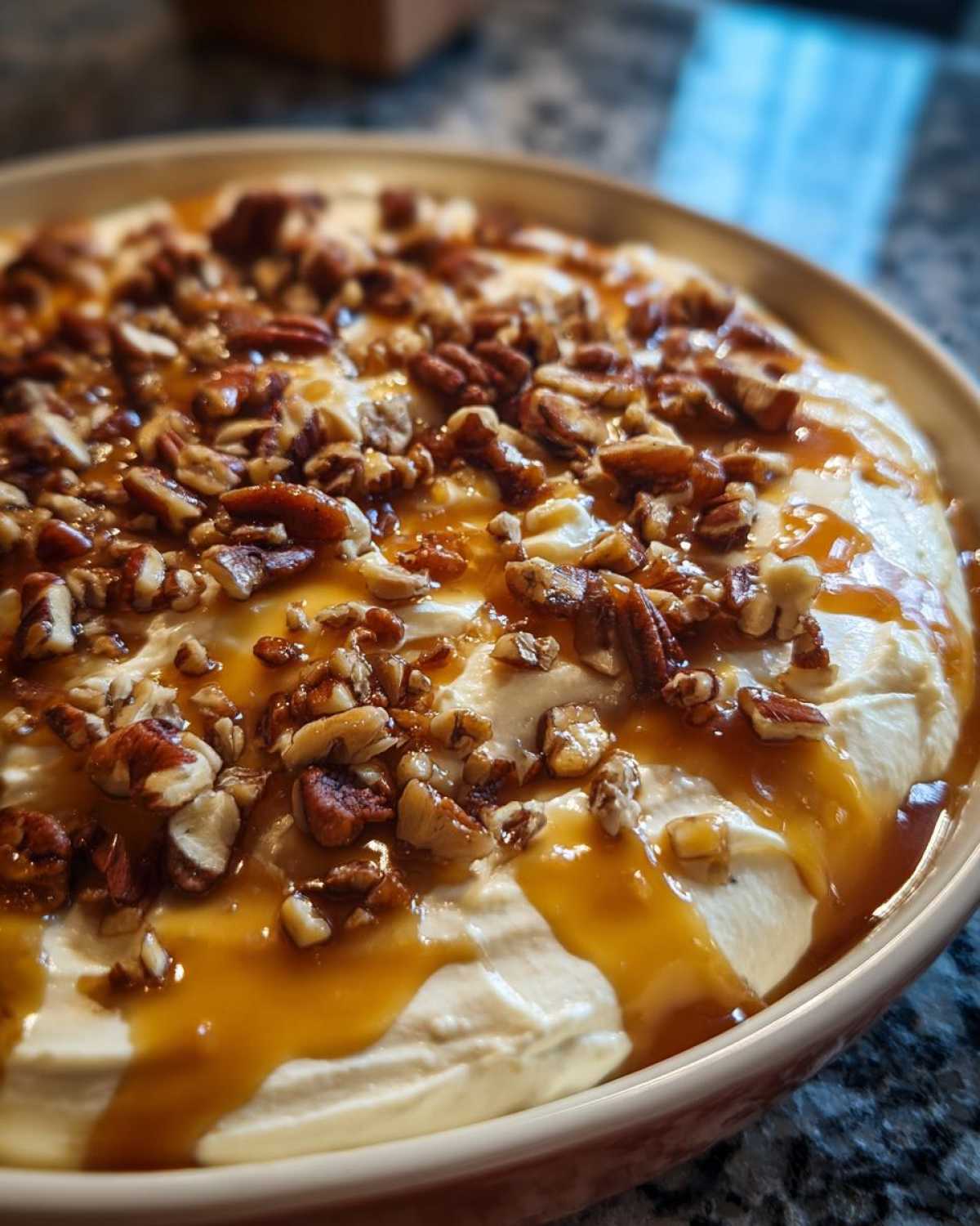 A close-up of a creamy pecan pie dip topped generously with chopped pecans and drizzled with rich caramel sauce.