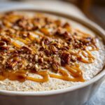 Close-up of creamy pecan pie dip topped with chopped pecans and a generous caramel sauce drizzle.
