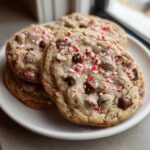 A stack of freshly baked peppermint chocolate chip cookies topped with chocolate chips and crushed candy canes.