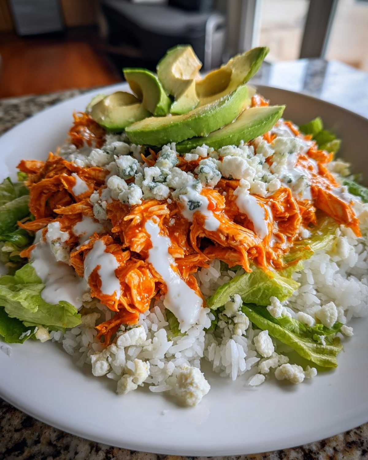Close-up of a delicious buffalo chicken bowl featuring shredded orange buffalo chicken, white rice, lettuce, blue cheese crumbles, and sliced avocado.