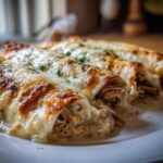 Close-up of three baked white chicken enchiladas covered in melted, slightly browned cheese and parsley.