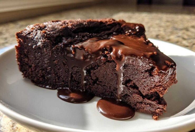 A dense slice of flourless chocolate cake topped with dripping chocolate ganache, served on a white plate.