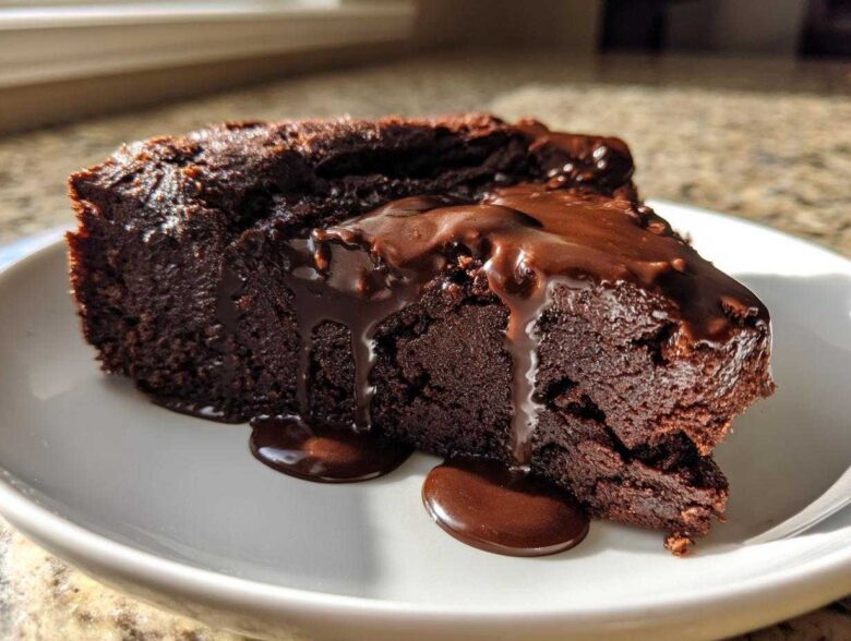 A dense slice of flourless chocolate cake topped with dripping chocolate ganache, served on a white plate.