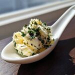 A scoop of homemade garlic butter mixed with fresh green herbs served on a white ceramic spoon.