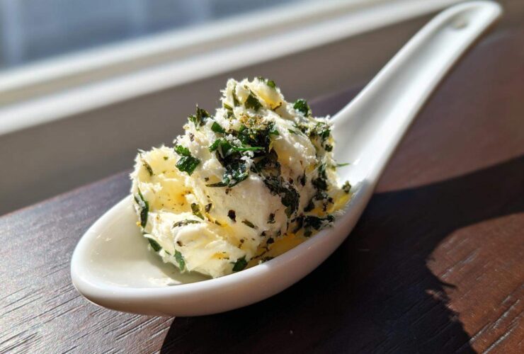 A scoop of homemade garlic butter mixed with fresh green herbs served on a white ceramic spoon.