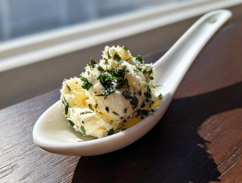 A scoop of homemade garlic butter mixed with fresh green herbs served on a white ceramic spoon.