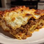 Close-up of a thick, layered slice of sheet pan lasagna with rich meat sauce and bubbly, browned cheese topping.