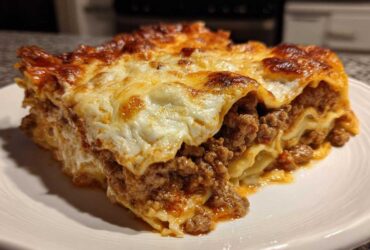 Close-up of a thick, layered slice of sheet pan lasagna with rich meat sauce and bubbly, browned cheese topping.