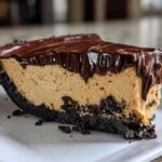 A close-up slice of rich peanut butter pie with a dark chocolate crust and thick chocolate ganache topping.