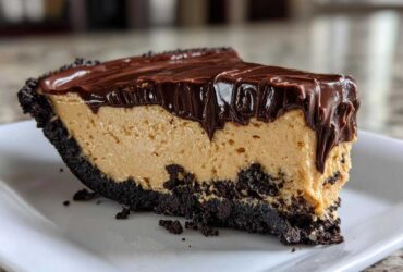 A close-up slice of rich peanut butter pie with a dark chocolate crust and thick chocolate ganache topping.