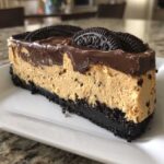 A thick slice of no-bake peanut butter pie featuring a dark cookie crust, creamy peanut butter filling, chocolate ganache, and whole Oreo cookies.