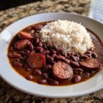 A white bowl filled with rich, saucy slow cooker red beans and rice, topped with slices of smoked sausage.