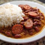 Close-up of a white plate featuring slow cooker red beans and rice topped with slices of smoked sausage.