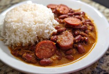 Close-up of a white plate featuring slow cooker red beans and rice topped with slices of smoked sausage.
