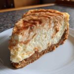 A thick slice of creamy snickerdoodle cheesecake with a graham cracker crust, dusted with cinnamon.