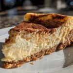 A thick slice of creamy snickerdoodle cheesecake with a graham cracker crust, dusted heavily with cinnamon.