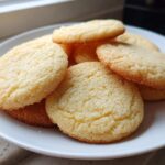 A stack of soft and chewy sugar cookies with a slightly crisp, sugared top, resting on a white plate.