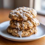 Three soft iced oatmeal cookies stacked on a white plate, drizzled with white vanilla icing.