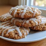 A stack of soft iced oatmeal cookies drizzled with white vanilla icing on a white plate.