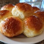 A cluster of six shiny, golden brown sourdough discard rolls baked together on a white plate.