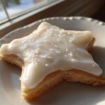 A star-shaped sugar cookie topped with thick, glossy white sugar cookie icing and fine white sprinkles.