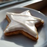 Close-up of a star-shaped sugar cookie topped with thick, glossy white sugar cookie icing on a white plate.