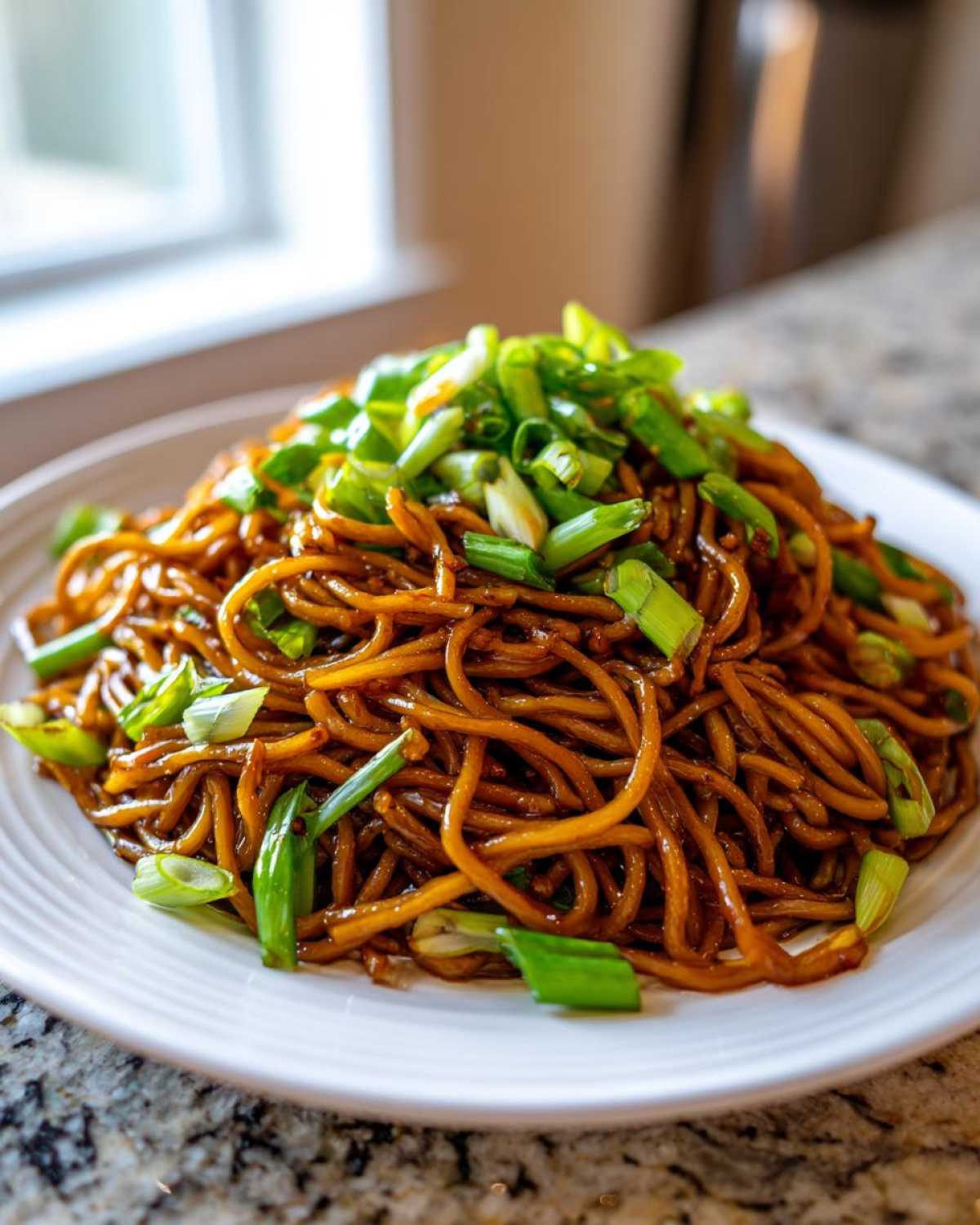 A close-up of a plate piled high with sticky garlic noodles, generously topped with bright green sliced scallions.