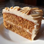 A close-up of a moist slice of spice cake layered with frosting, sitting on a white plate.