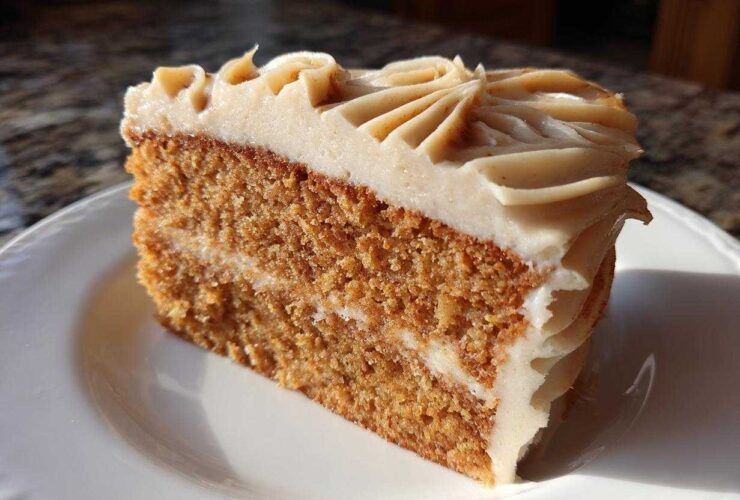 A close-up of a moist slice of spice cake layered with frosting, sitting on a white plate.