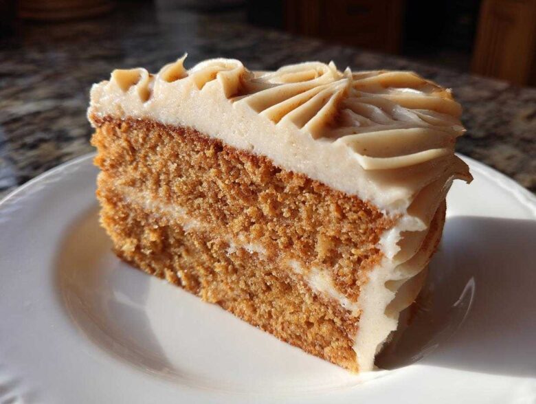 A close-up of a moist slice of spice cake layered with frosting, sitting on a white plate.
