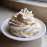 A beautiful swirl of fluffy, creamy vanilla buttercream frosting piped onto a small white dish.