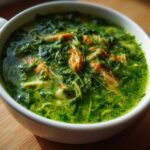 Close-up of a vibrant green chicken poblano soup, showing shredded chicken and leafy greens in a white mug.