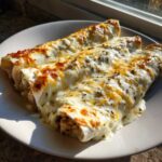 Three rolled white chicken enchiladas covered in melted white cheese and green herbs on a white plate.