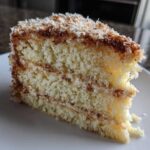 Close-up of a moist slice of white German chocolate cake showing layers and toasted coconut pecan frosting.