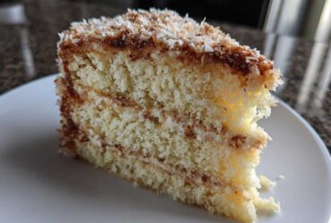 Close-up of a moist slice of white German chocolate cake showing layers and toasted coconut pecan frosting.