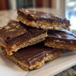 Close-up of stacked squares of graham cracker toffee featuring a crunchy base, gooey caramel layer, and rich chocolate topping.