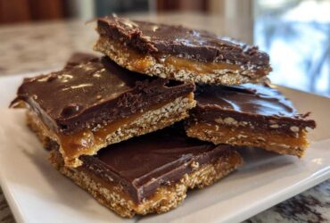 Close-up of stacked squares of graham cracker toffee featuring a crunchy base, gooey caramel layer, and rich chocolate topping.