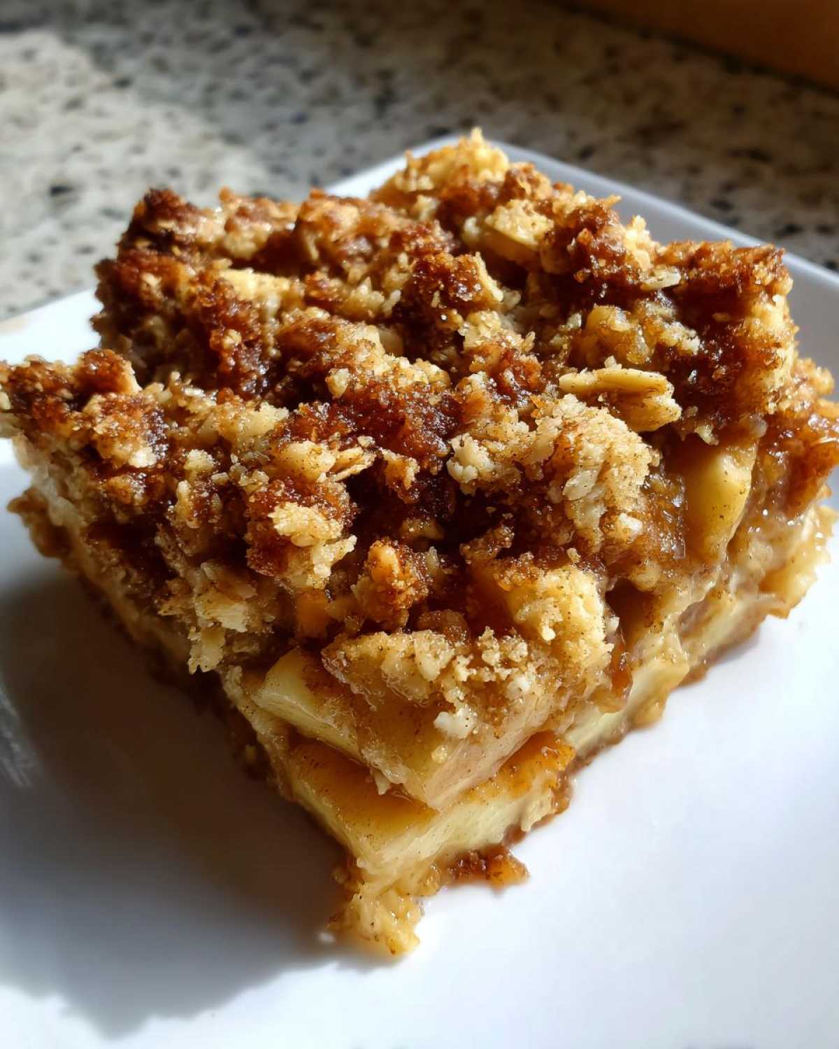 Close-up of a square serving of apple crisp recipe showing thick, tender apple slices and a rich, brown, crunchy oat topping.