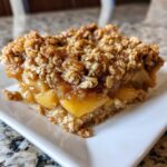 A close-up of a square serving of amazing apple crisp recipe with gooey apples and crunchy oat topping.