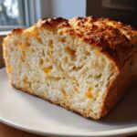 Cross-section of a loaf of amazing beer bread showing a soft, airy crumb dotted with melted cheddar cheese pieces.