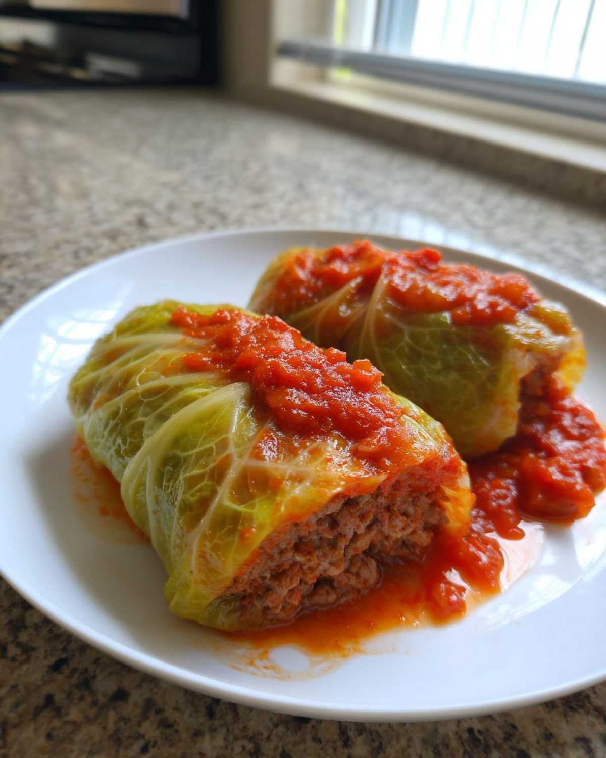 Two stuffed cabbage rolls topped with tomato sauce served on a white plate, showing the meat filling of the cabbage rolls.
