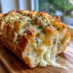 Close-up of freshly baked cheese bread with melted cheese strings pulling apart, topped with herbs.