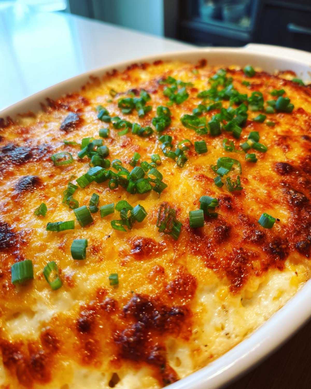 Close-up of a baked, creamy corn dip topped with bubbly, browned cheese and fresh green onions.