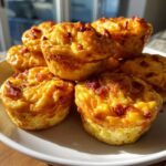 A stack of golden brown, baked egg bites topped with bacon pieces, highlighting the fluffy texture.