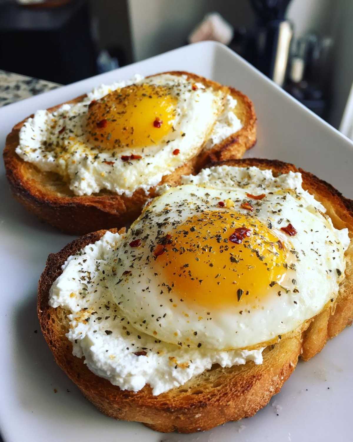 Two slices of amazing egg toast topped with creamy ricotta cheese and seasoned fried eggs.
