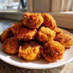 A mound of golden brown, crispy fried okra pieces piled high on a white plate, illuminated by natural light.