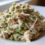 A mound of creamy, shredded honey mustard chicken salad mixed with celery and green onions on a white plate.
