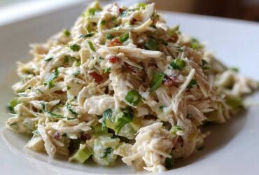 A mound of creamy, shredded honey mustard chicken salad mixed with celery and green onions on a white plate.