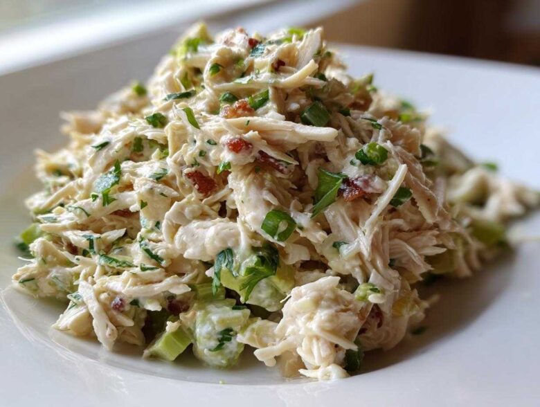 A mound of creamy, shredded honey mustard chicken salad mixed with celery and green onions on a white plate.