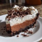 A decadent slice of multi-layered mud pie with chocolate crust, mousse filling, whipped cream, and chocolate shavings.